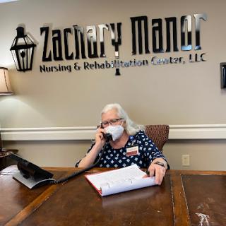 A receptionist at Zachary Manor Nursing & Rehabilitation Center assists a caller while adhering to health protocols.