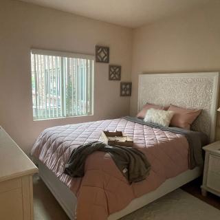 A cozy bedroom with soft pink bedding and natural daylight.