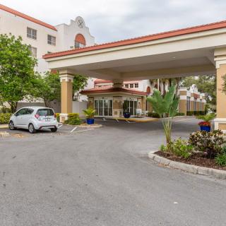 A hotel entrance featuring a driveway with a parked car and surrounding landscaping.