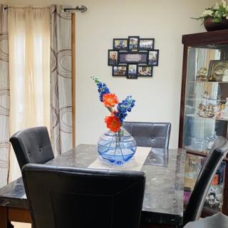 A cozy dining room featuring a table with a decorative vase and flowers, surrounded by chairs and adorned with wall picture frames.