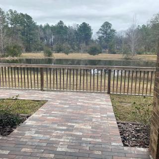 A view of a serene lake from a brick patio, surrounded by trees and fenced with wooden rails.