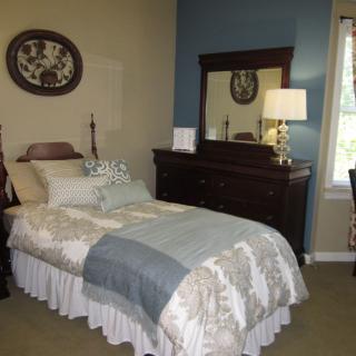 A cozy bedroom with a single bed and a wooden dresser beside a window.