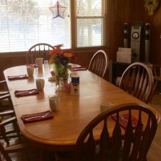 A cozy dining room with a wooden table set for breakfast, featuring flowers as a centerpiece.