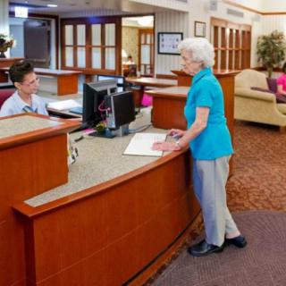 A senior woman interacting with a staff member at a reception desk.
