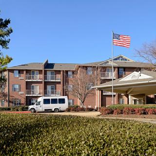 A brick building with a transport van parked nearby and an American flag flying under a clear blue sky.