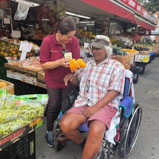 A friendly interaction at a local market, where a vendor helps a customer in a wheelchair.