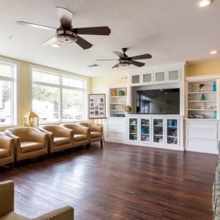 A spacious living room featuring comfortable seating, ceiling fans, and ample natural light from large windows.