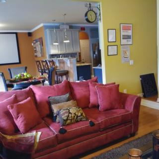 A cozy living room with a vibrant red sofa and an open-plan kitchen in the background, showcasing colorful walls and modern decor.