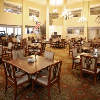 A spacious dining area with elegantly arranged tables and chairs, featuring chandeliers and flags.