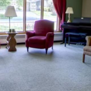 A cozy living room with a red armchair, a lamp, and a piano near the window.