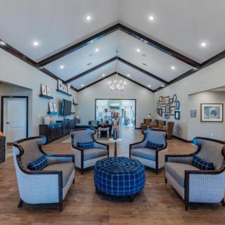 A spacious living room with modern furniture and a vaulted ceiling, featuring a central seating area and elegant lighting.