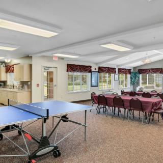 A spacious community room featuring a ping pong table and a large meeting area with tables and chairs.