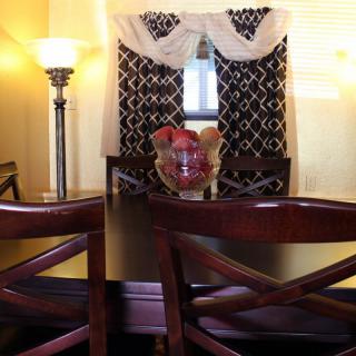 A cozy dining room featuring a dark wood table and chairs, illuminated by a floor lamp with decorative curtains in the background.