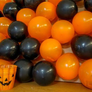 A festive arrangement of orange and black balloons alongside a Halloween-themed pumpkin bucket.