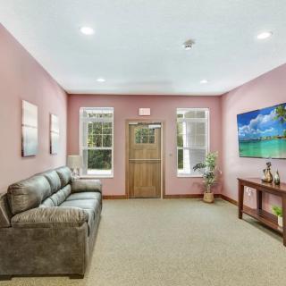 A cozy living room with pink walls, featuring a comfortable sofa, wall art, and natural lighting from large windows.