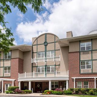 A multi-story residential building with brick and siding exterior under a partly cloudy sky.