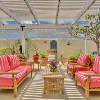 A cozy outdoor patio with red cushioned seating under a pergola, surrounded by plants.