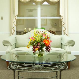 A cozy living room with a light-colored sofa, a glass coffee table, and a vibrant floral arrangement.