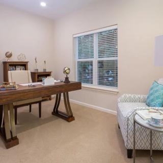 A neatly organized home office with a large wooden desk and an armchair by the window.