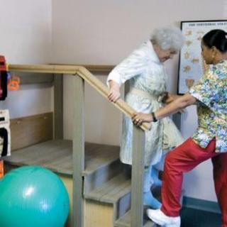 A caregiver assists an elderly person with physical therapy exercises.