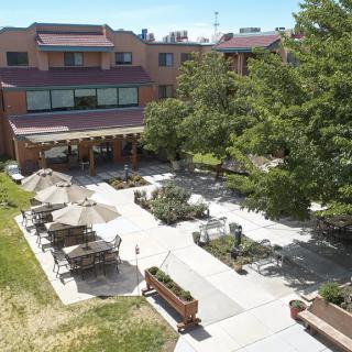 Aerial view of a courtyard with tables and umbrellas surrounded by trees and a building.