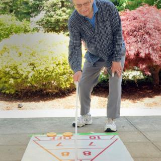 An elderly person playing a game of shuffleboard outdoors.