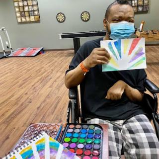A person in a wheelchair showcases their colorful painting, highlighting the power of creative expression through art therapy.