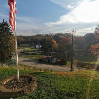 A scenic view of a countryside road lined with autumn trees and an American flag under a bright sky.