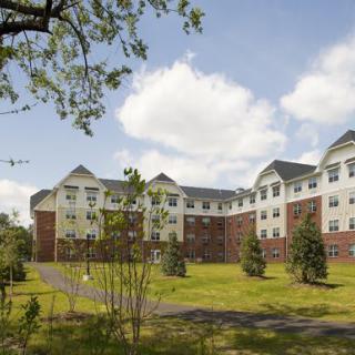 A large residential building with a well-maintained lawn and trees under a partly cloudy sky.