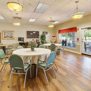 A well-lit dining area with round tables and green chairs, featuring a welcoming atmosphere.