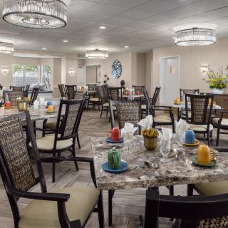 A well-decorated dining area with multiple tables and chairs, featuring modern chandeliers and colorful table settings.