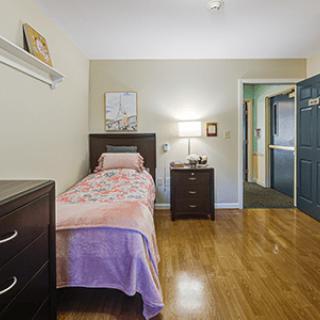 A cozy bedroom with a single bed, nightstand, and dresser on a hardwood floor.