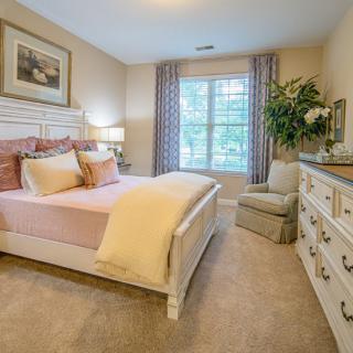 A cozy and elegantly decorated bedroom with a large bed, dresser, and window providing natural light.