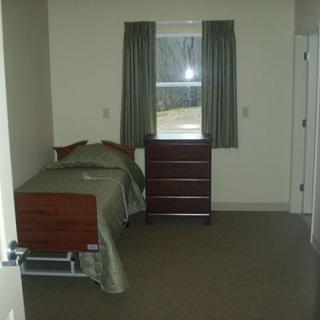 A minimalist bedroom with a single bed and a dresser under a window with green curtains.