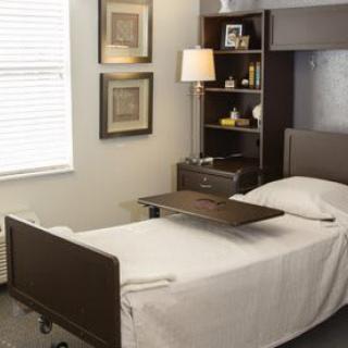 A well-organized room featuring a hospital bed with an over-bed table, a shelf, and a window.