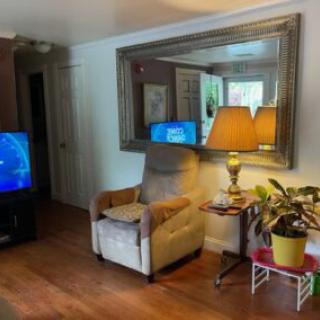 A cozy living room featuring an armchair, a large mirror, a lamp, and a television.