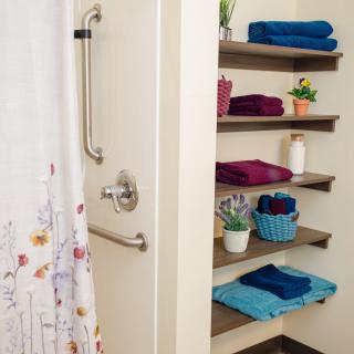A neatly organized bathroom with colorful towels on shelves and a shower area.