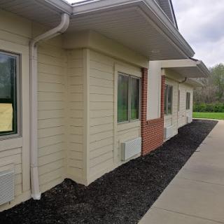 A corner view of a modern building with light siding and a landscaped area.