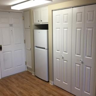 A small kitchen area featuring a refrigerator and storage closets with a warm wooden floor.