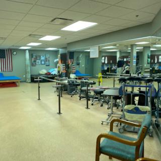 An interior view of a rehabilitation center featuring exercise equipment, chairs, and mirrors.