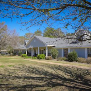 A picturesque single-story ranch house surrounded by trees and a clear blue sky.