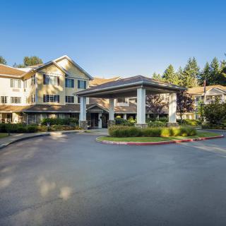 A sunny view of a building with a landscaped entrance and surrounding trees.