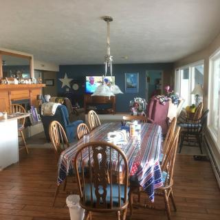 A spacious dining and living area featuring wooden furniture, large windows, and a television.