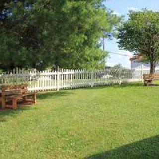 A peaceful garden with a white picket fence, benches, and lush green grass.