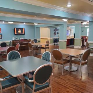 A cozy indoor dining area with tables, chairs, and a television, featuring soft lighting and inviting decor.
