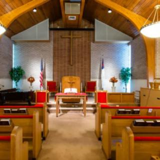Interior of a church with wooden pews, an altar, and a large cross.