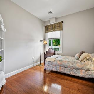 A cozy bedroom with a single bed, wooden floors, and a bookshelf near the window.