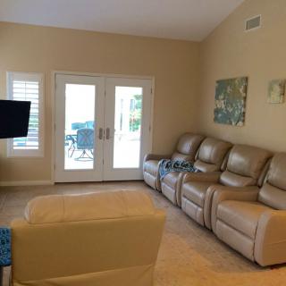 A cozy living room with beige leather recliners, a mounted TV, and natural light streaming through French doors.