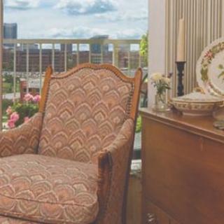 A cozy vintage armchair by a window with classic decor and a view of the garden outside.