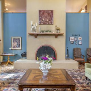A cozy living room featuring a stylish fireplace, wooden coffee table with a flower vase, surrounded by blue walls and decorative artwork.
